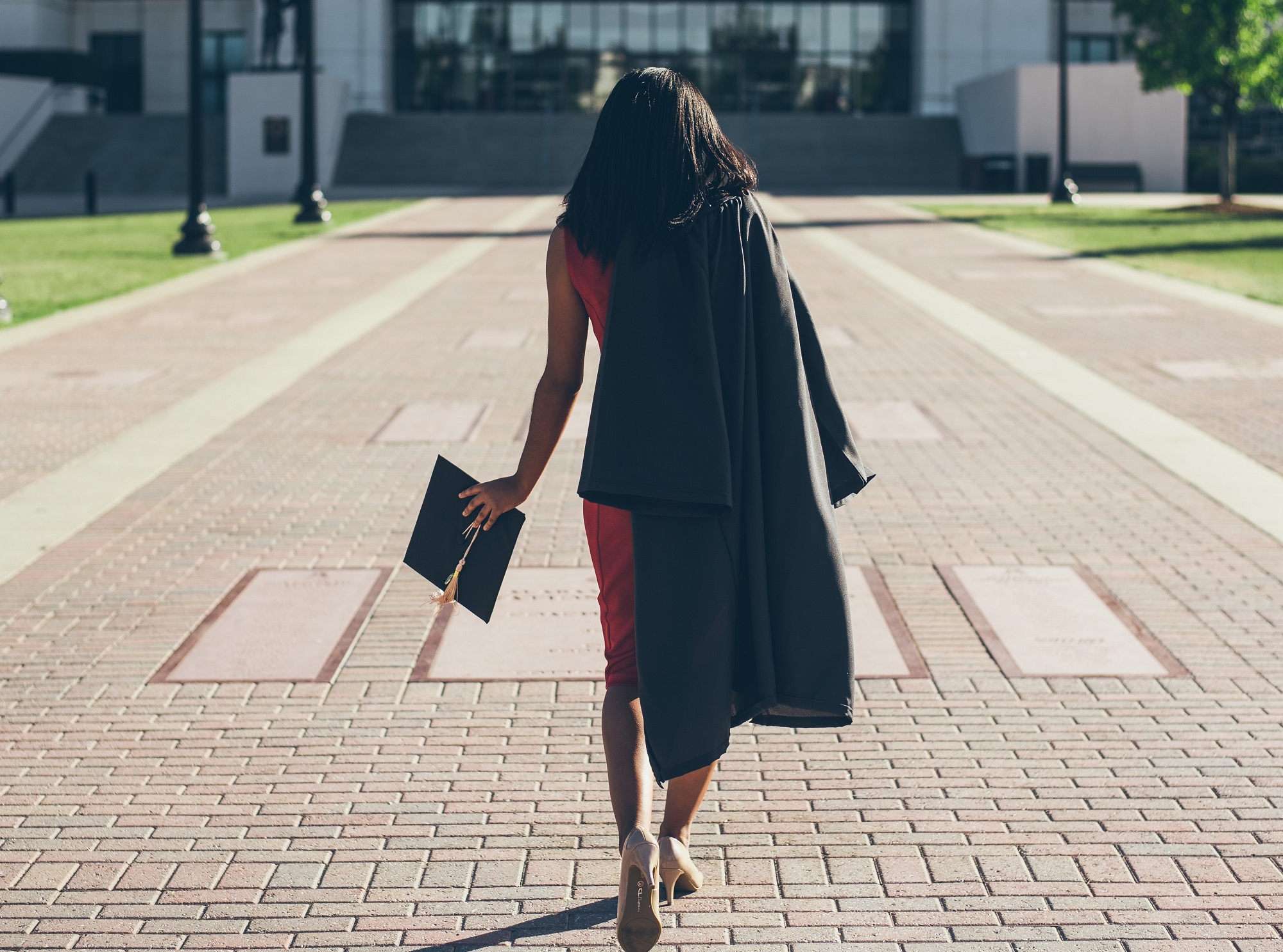 mujer independiente que lleva su toga de graduación caminando hacia un edificio donde puede comenzar su carrera tecnológica