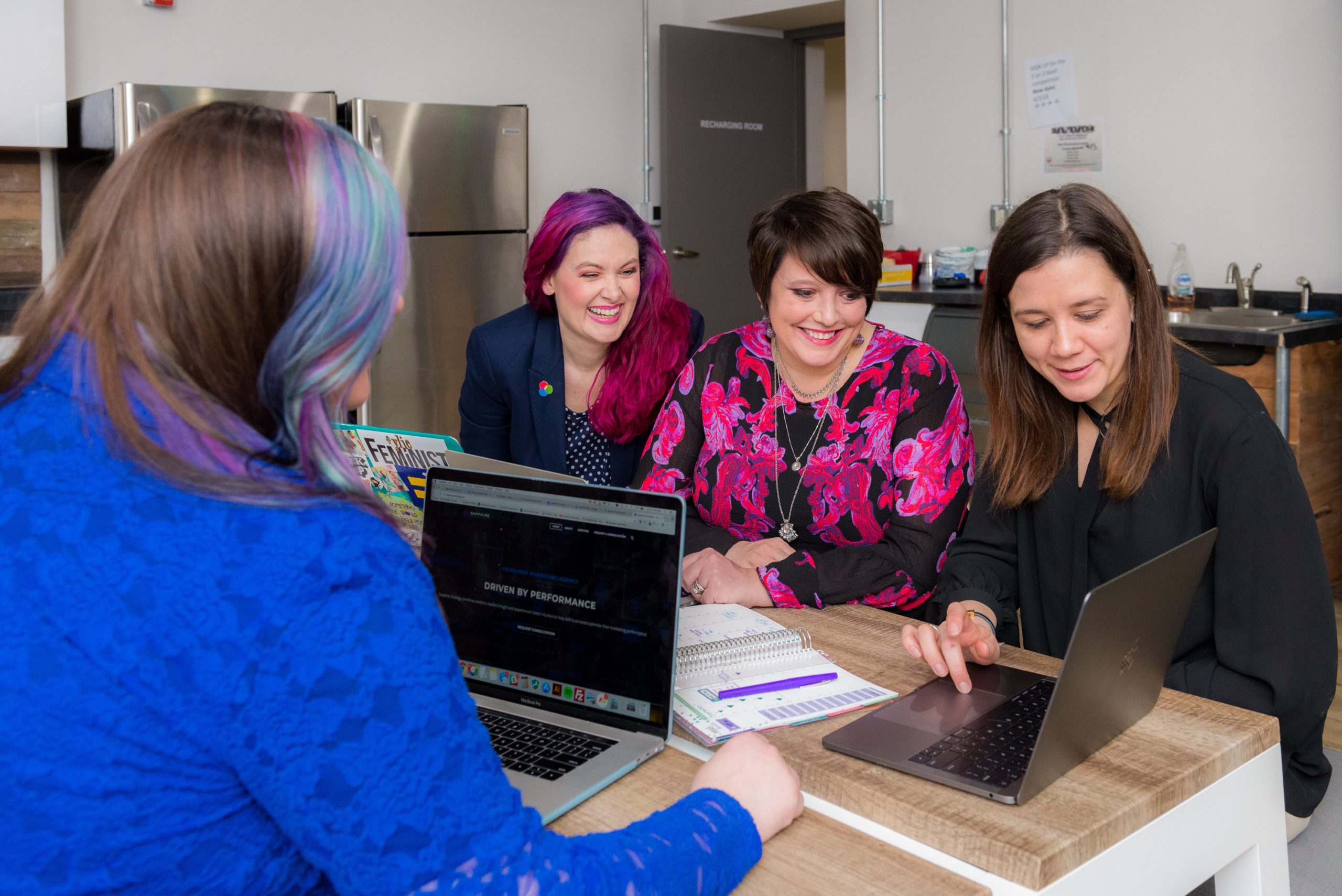 cuatro mujeres independientes discutiendo juntas algo que una de ellas está presentando desde una computadora portátil mientras marcan la diferencia en su carrera tecnológica