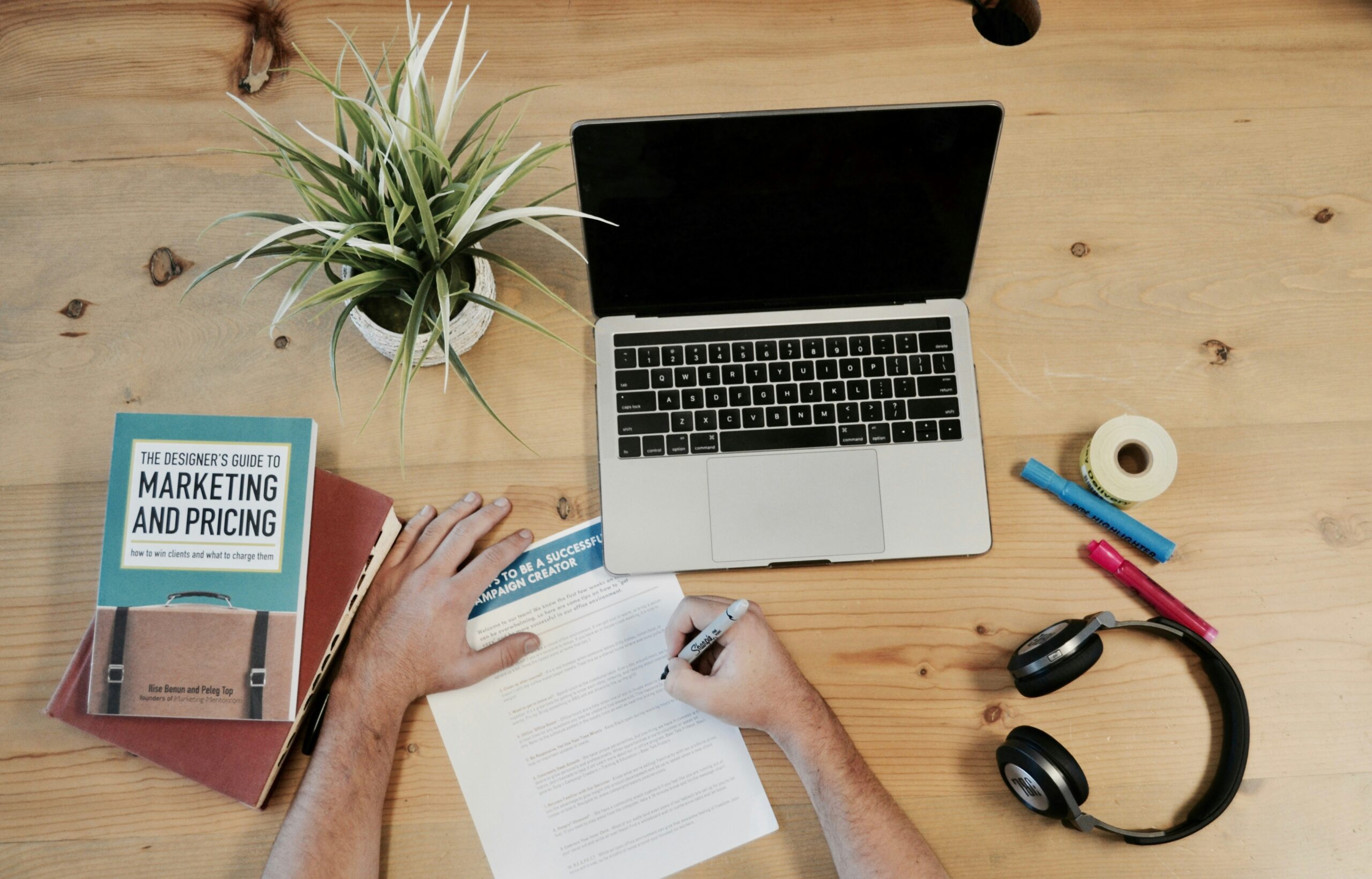 person writing on notepad on desk with computer and marketing book