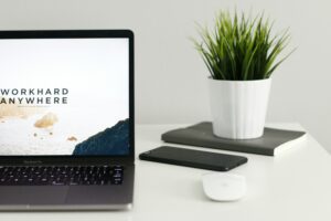 laptop on a desk with a phone, mouse, and plant, the laptop is open to a freelancer platform page that says work hard anywhere
