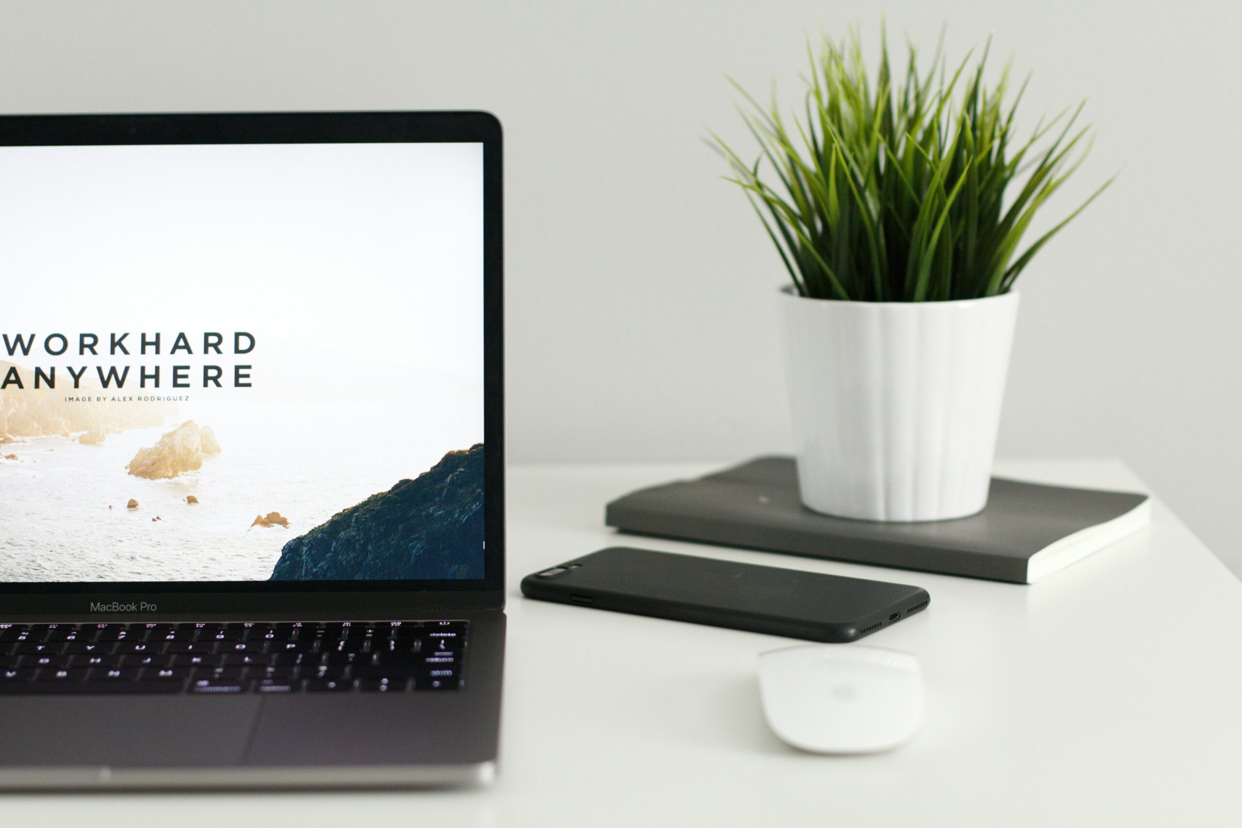 laptop on a desk with a phone, mouse, and plant, the laptop is open to a freelancer platform page that says work hard anywhere