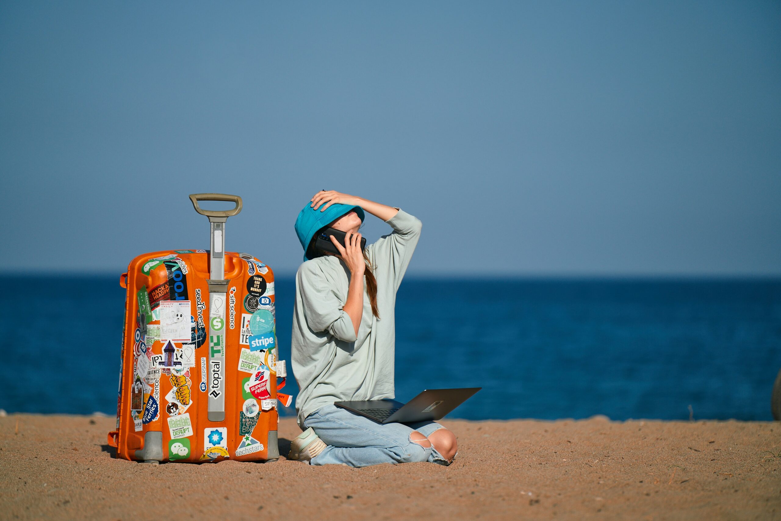 freelancer with orange suitcase on their phone and laptop at the beach during the summer