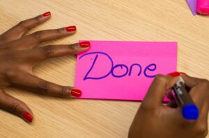 Black hands with pink polish writing done on a pink notecard