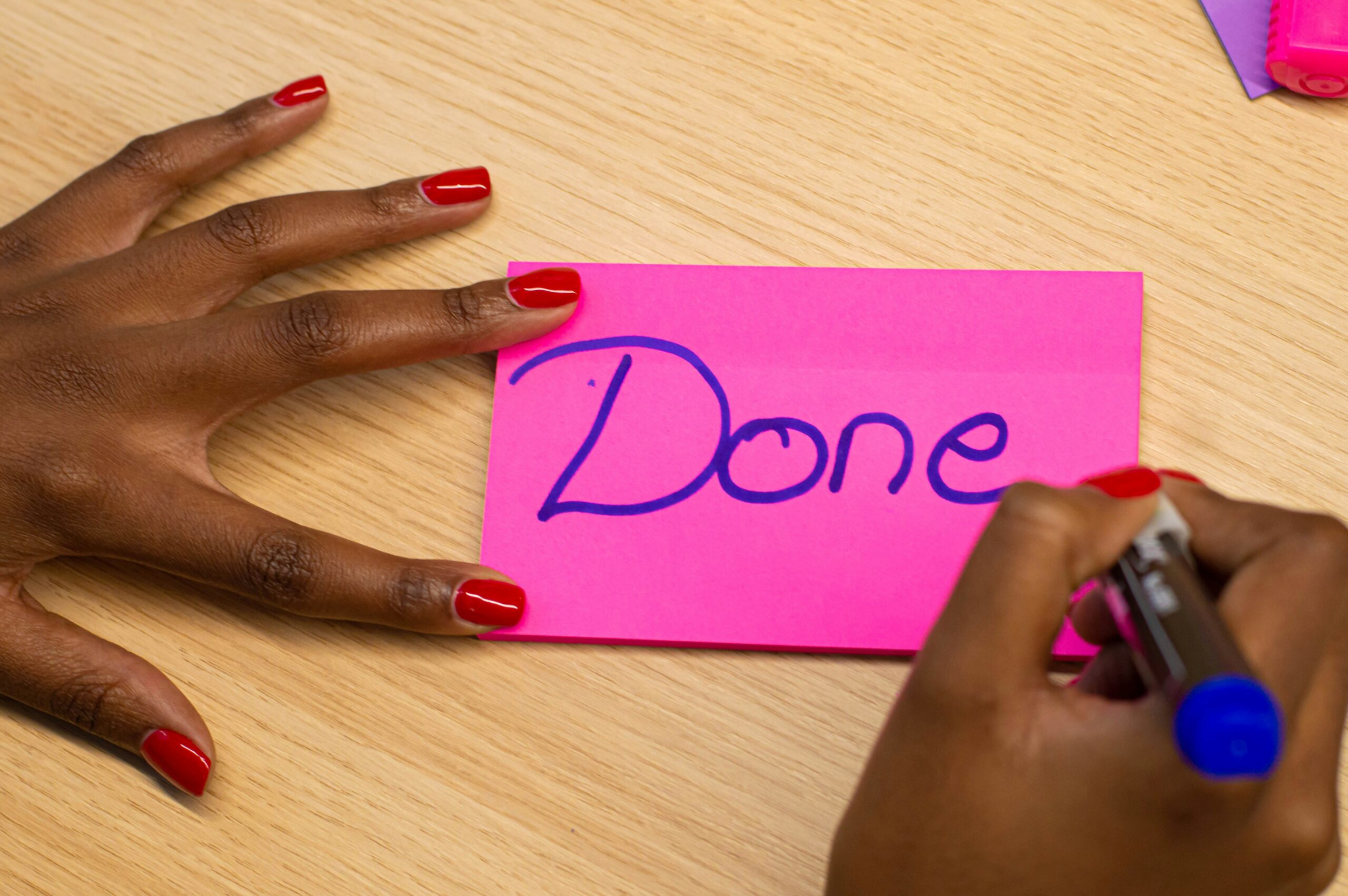 Black hands with pink polish writing done on a pink notecard
